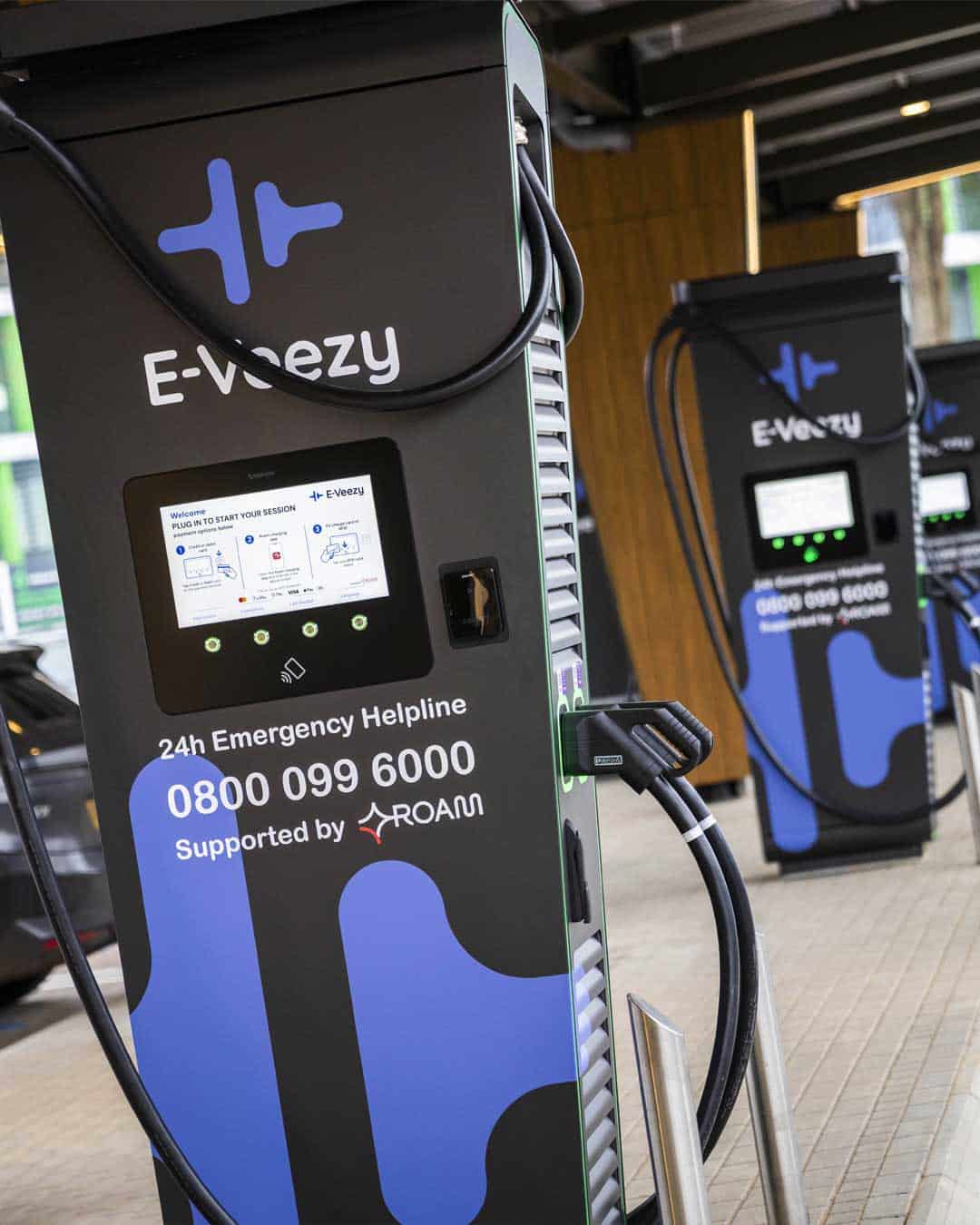 E‑Veezy electric vehicle charging station with digital interface, contactless payment, and emergency helpline.